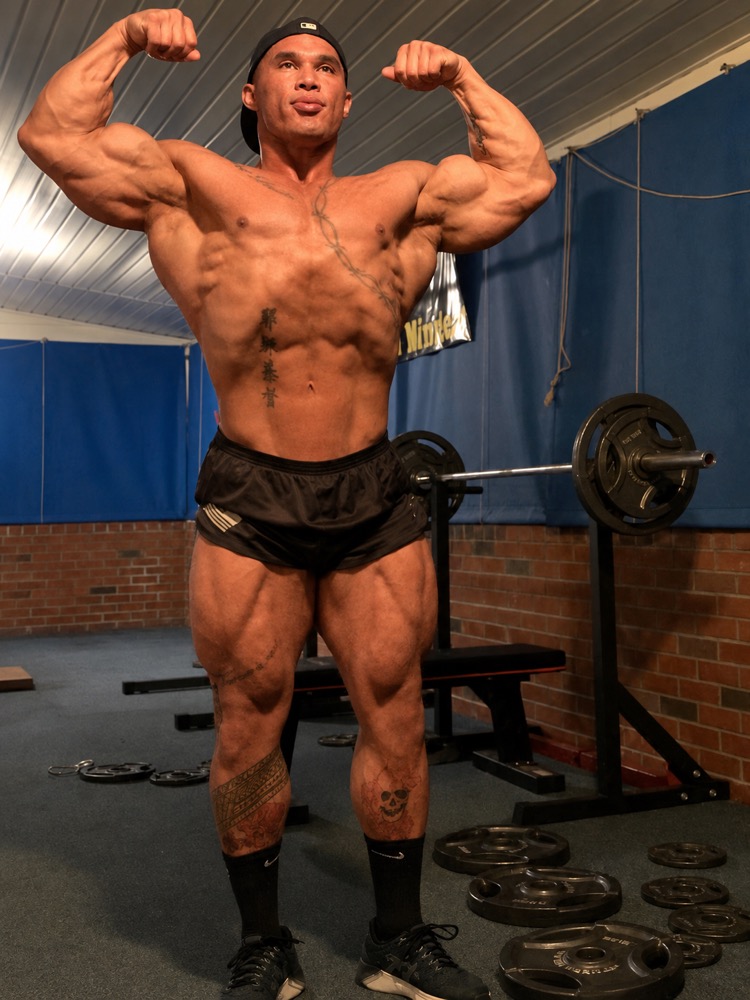 Nam Thomas Shartzer flexing in a garage powerlifting gym